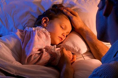 Niña durmiendo en la cama, con su papá sosteniéndole una mano y su otra mano sobre la cabeza de la niña. Una ilustración del cuidado de Dios expresado en el Salmo 121